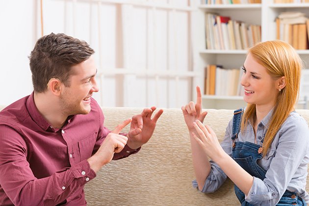 Smiling young woman talking using sign language with her hearing impairment man